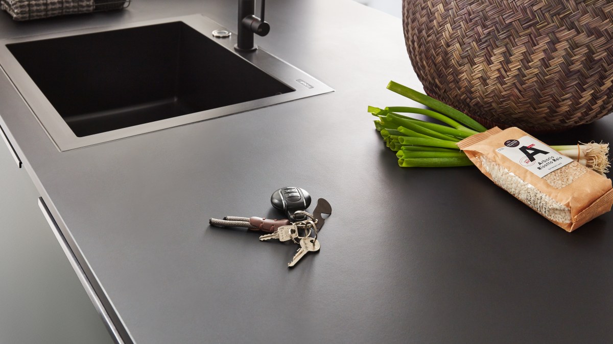 Dunkle Arbeitsplatte mit flächenbündig eingebauter schwarzer Spüle, daneben Frühlingszwiebeln und eine Packung Risottoreis