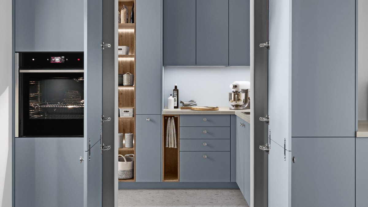 Blick durch geöffnete Türen in eine Küche mit blaugrauen Fronten, beleuchteten Vorratsregalen in Holzoptik und Backofen im Hochschrank